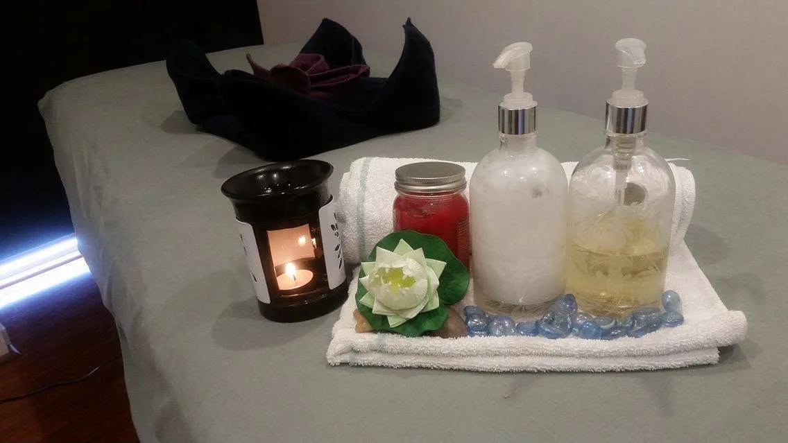 Treatment-table detail: lit candle, white lotus, massage oils and blue glass stones