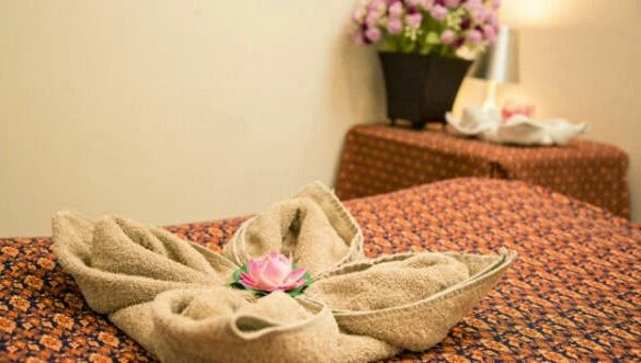 Massage bed dressed in orange-red Thai-print fabric with a folded-towel lotus and pink flowers